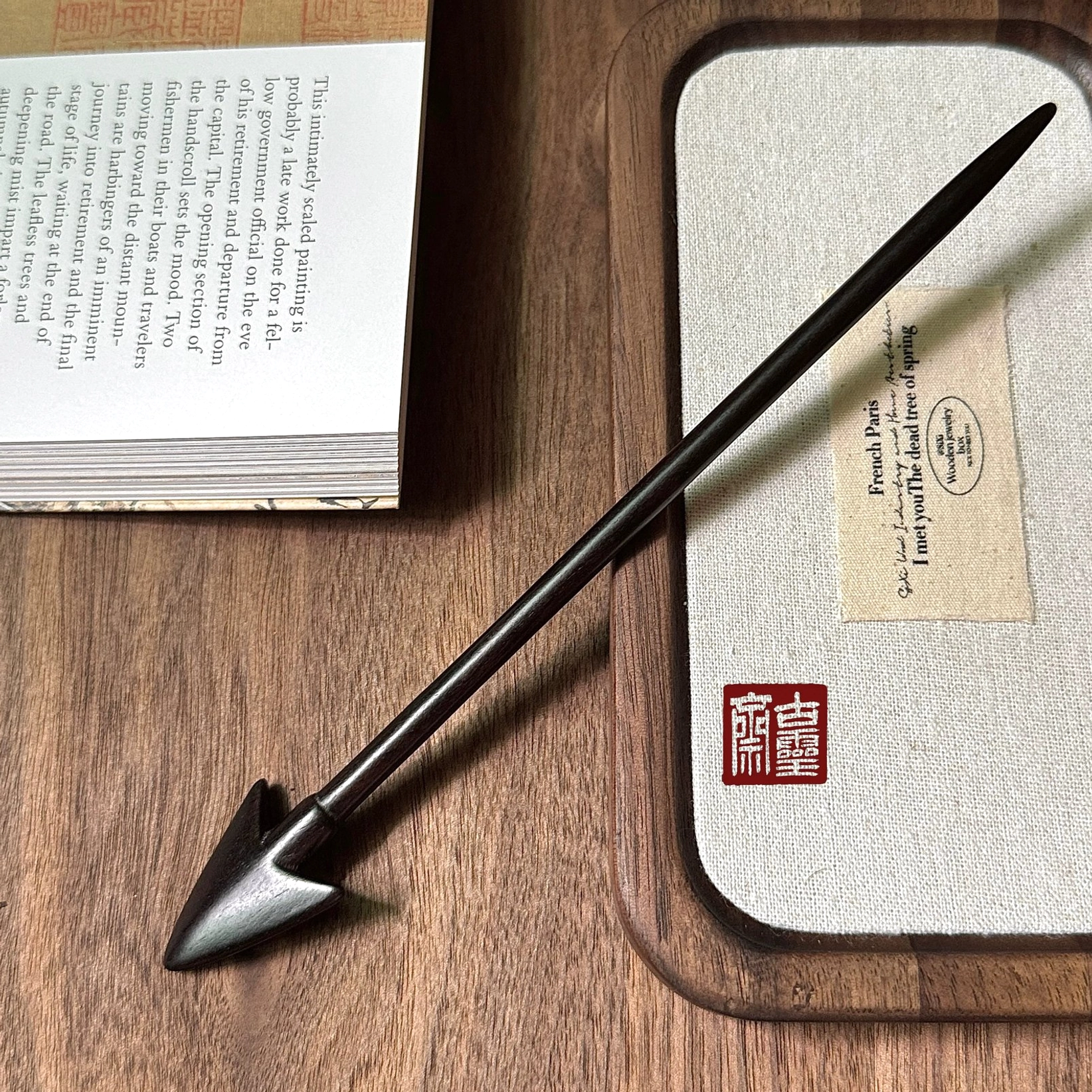 Side view of a polished matte black traditional Chinese arrow hair stick on a wooden tabletop with book and tray props