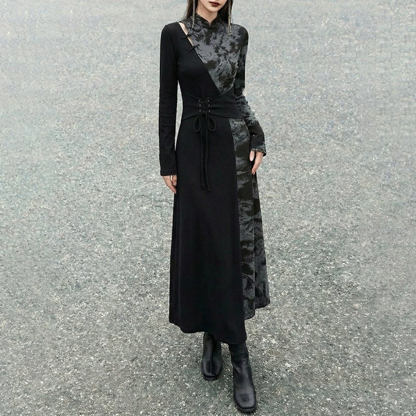 Rear side view of a black asymmetric modern Chinese dress with shoulder cutout, tie-dye side panels, long sleeves, floor-length skirt, and black ankle boots