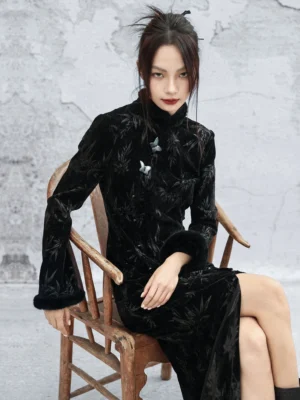 Black bamboo leaf jacquard velvet cheongsam dress shown in a three-quarter seated view with stand collar, frog buttons, fitted silhouette, and fluffy black cuffs