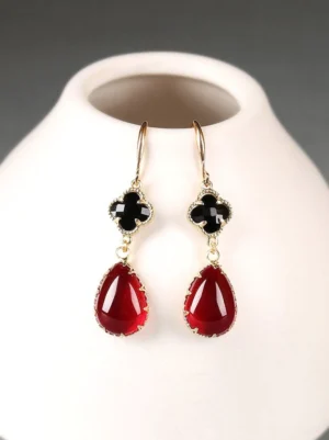 Close-up of elegant black and burgundy four-leaf clover Chinese earrings with gold-toned hardware against a dark gray background