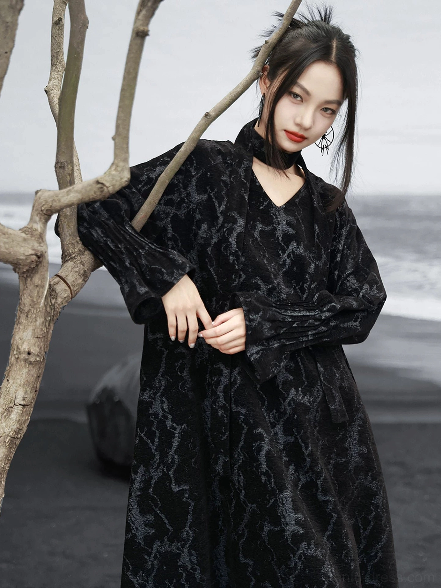 Black chenille jacquard modern Hanfu loose maxi dress with V-neck halter sash, flared sleeves, and relaxed silhouette shown on a model at a black sand beach