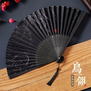 Black Chinese folding fan with silver willow branches and cloud painting, hollow carved ribs, red seal accent, and black tassel displayed with Chinese plum blossom decor