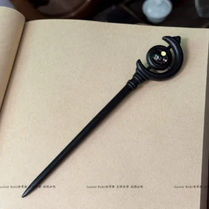 Matte black Chinese hair stick with crescent moon top and colored glass bead displayed on an open kraft paper notebook beside traditional tea accessories
