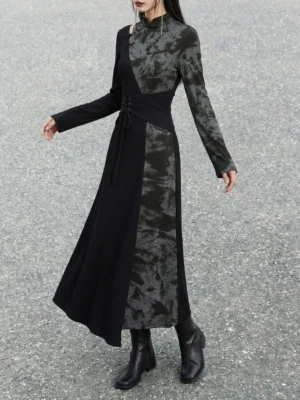 Side front view of a black Chinese-style contrast panel maxi dress with fitted long sleeves, asymmetric fabric splicing, stand collar, and floor-length silhouette