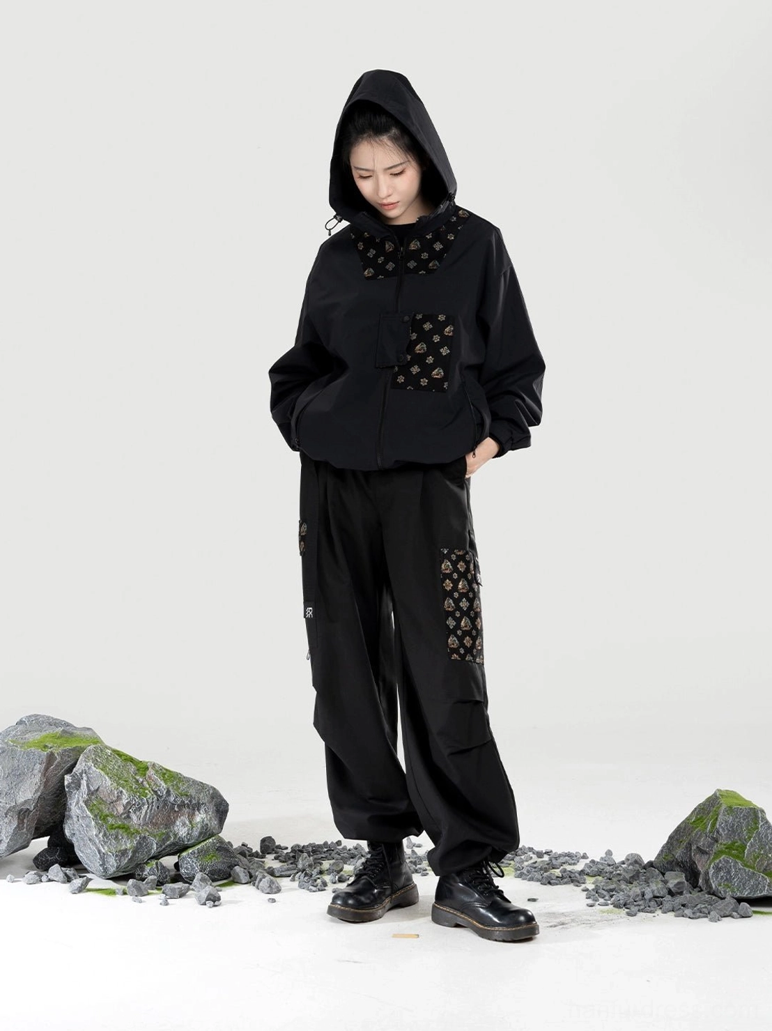 Black Chinese-style women’s hanfu outdoor set with hood worn up, relaxed cargo pants, large pockets, and decorative patterned patches