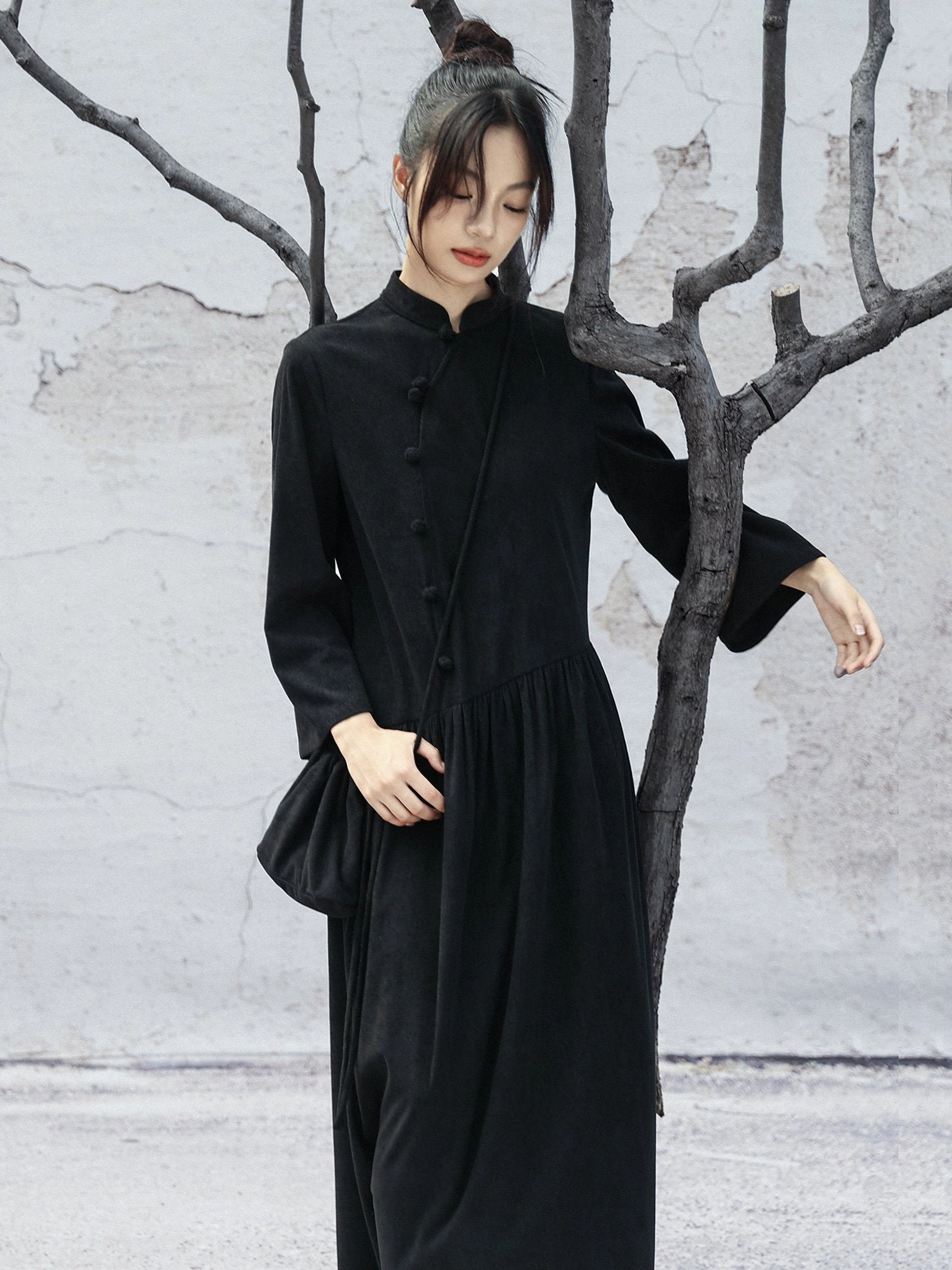 Three-quarter front view of a black corduroy-look Hanfu-inspired cheongsam dress with long sleeves, loose flowing skirt, and elegant gathered waist