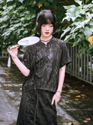 Black modern Hanfu short sleeve shirt with embroidered crane, asymmetrical frog buttons, stand collar, and tonal jacquard fabric styled with a matching skirt outdoors