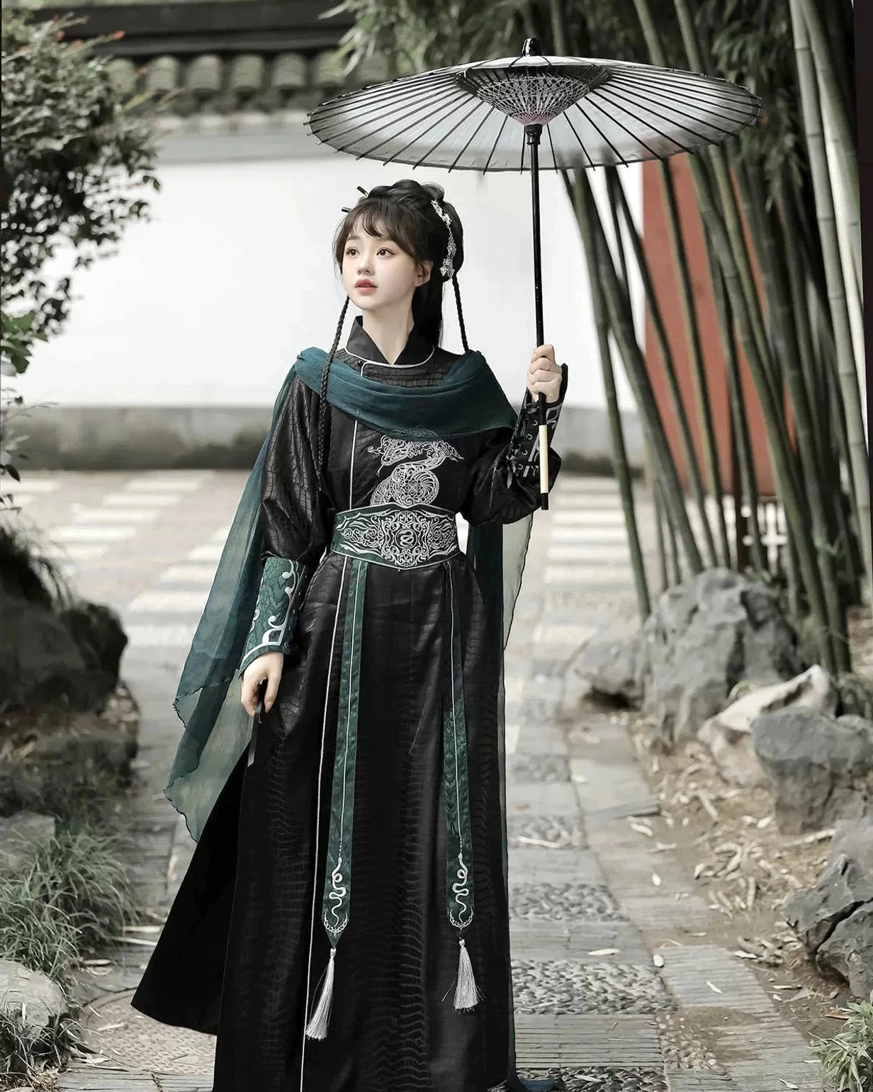 Female model wearing a black and dark green xianxia Hanfu costume with detailed silver waist embroidery and traditional Chinese bamboo paper umbrella