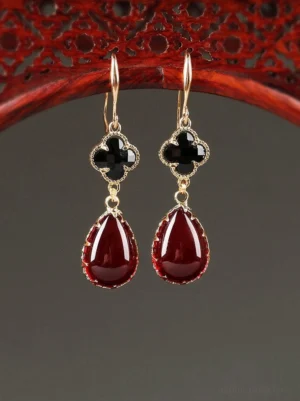 Four-leaf clover drop earrings with black faceted charms and burgundy teardrop pendants displayed on a carved Chinese red wood frame