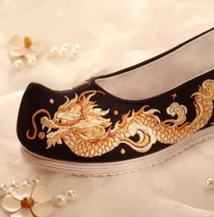 Side close-up of black traditional Chinese Hanfu shoe with detailed golden dragon embroidery, curved toe and white layered rubber sole