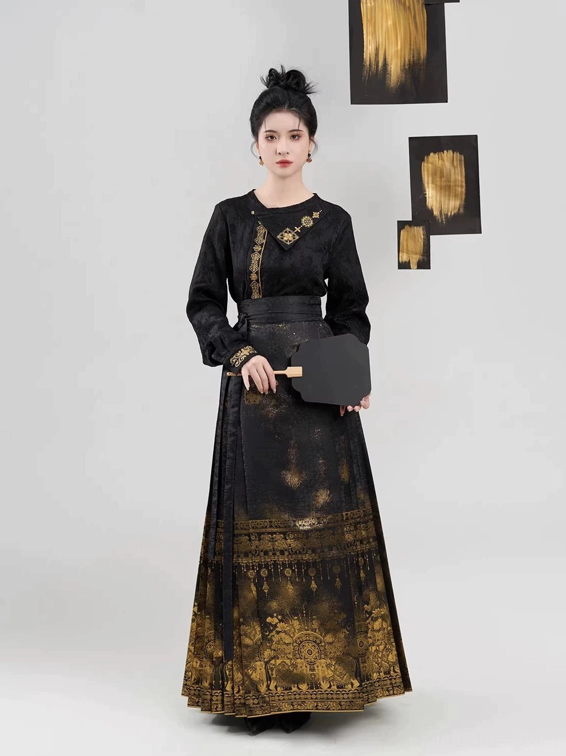 Front full-body view of black and gold Ming Dynasty Hanfu set featuring a jacquard long-sleeve top, pleated mamianqun skirt, and black folding fan