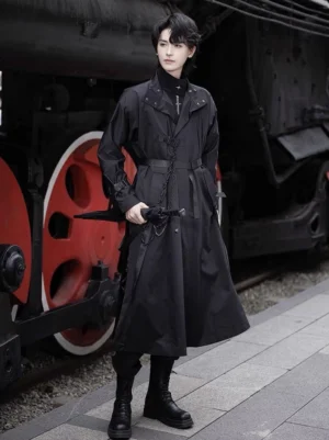 Full front view of a black gothic Hanfu robe coat with Tang-inspired round neck, waist cinching belt, cross neckline ornament, long sleeves, practical pockets, and combat boots beside a vintage steam train