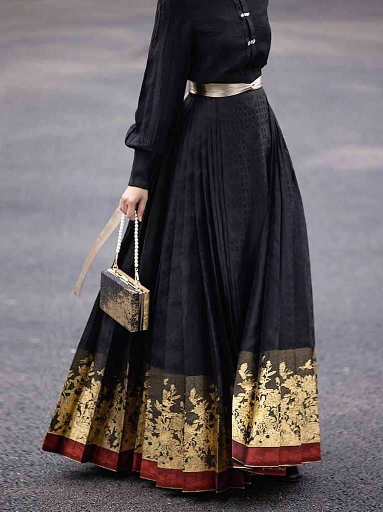 Close-up of a black Hanfu mamianqun skirt with subtle jacquard texture, gilded peony embroidery-style floral border, red trim, black top, and gold waist belt