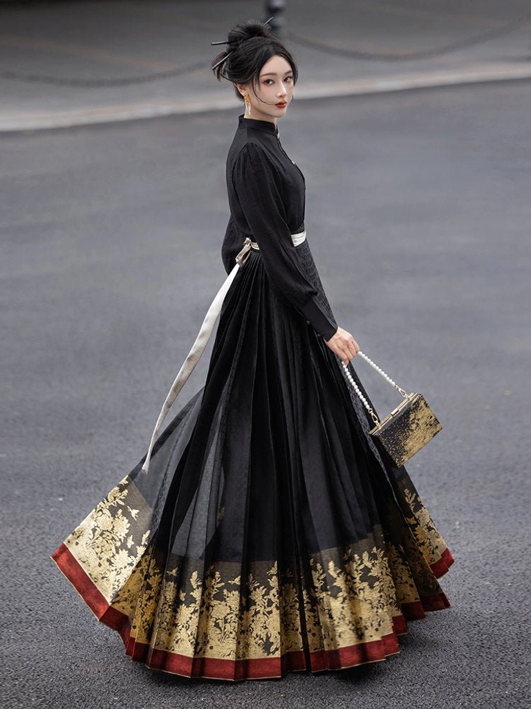 Side view of a model wearing a black Ming Dynasty Hanfu mamianqun skirt with pleated fabric, gilded peony floral hem, red trim, white waist sash, black top, and vintage handbag outdoors