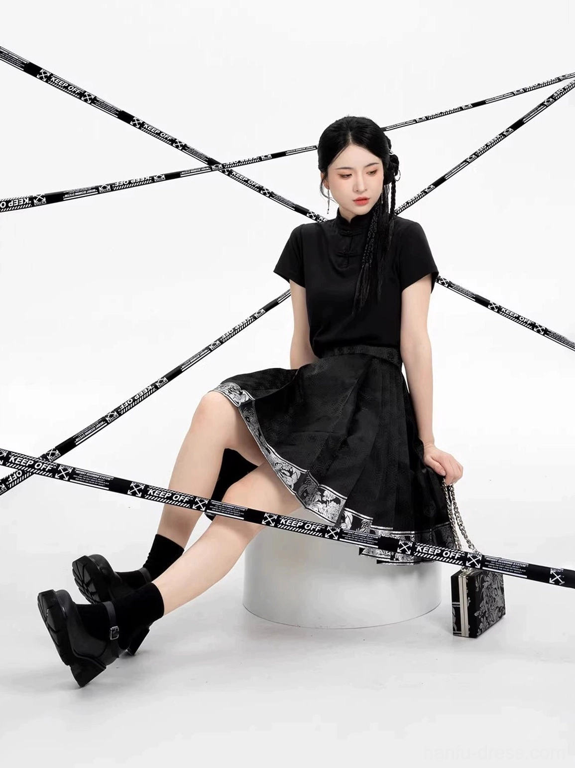 Seated side view highlighting the pleats and decorative woven hem of a black Ming-inspired mini mamian skirt