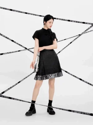 Three-quarter side view of a black mini mamian skirt styled with a Chinese-style top, black socks, platform loafers, and a chain handbag