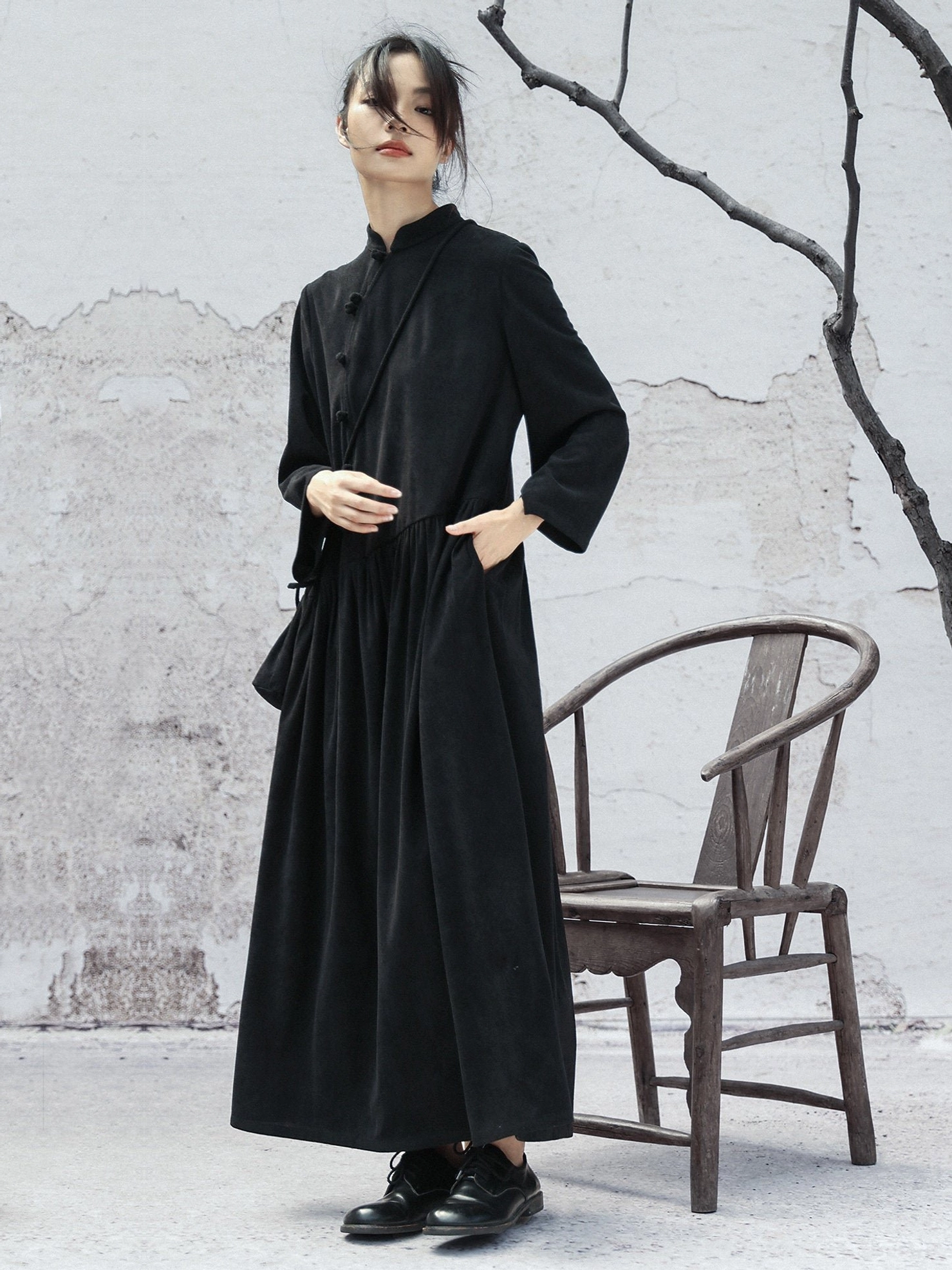 Side profile of a black modern Chinese cheongsam maxi dress with long sleeves, Mandarin stand collar, frog buttons, and softly ruched waist