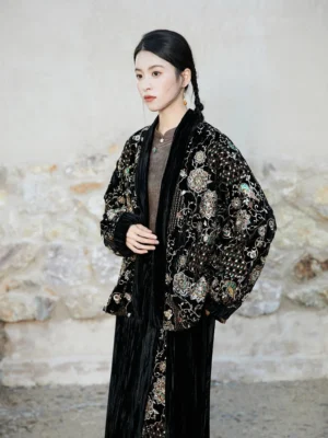 Front three-quarter view of black New Chinese Style oversized jacket with gold floral bead embroidery and velvet trimmed collar and cuffs