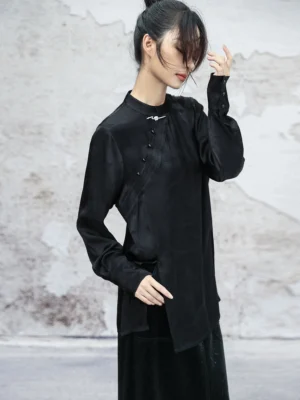 Side-front view of a black modern Hanfu satin top showing the asymmetric side hem, side slit, decorative frog button placket, and long sleeves