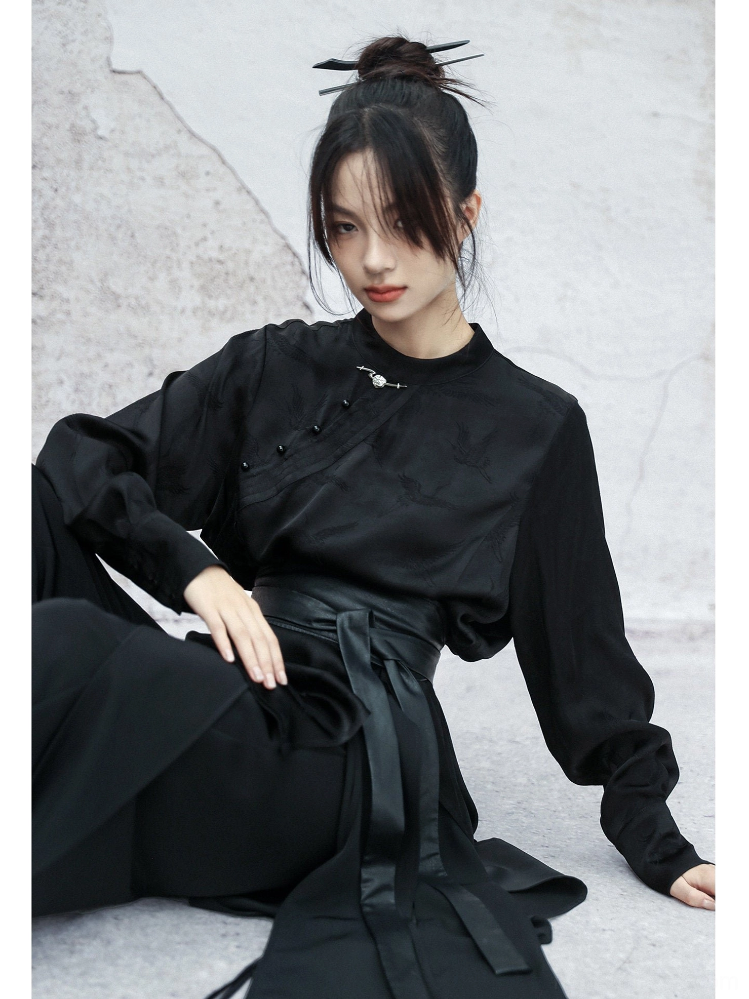 Close-up front view of a black modern Hanfu top displaying the stand collar, traditional frog buttons, tonal woven fabric pattern, and finished sleeve cuffs