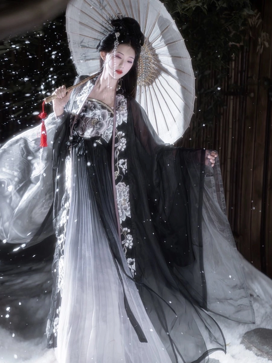 Full-length side view of Black Peony Tang style Heziqun Hanfu set in a snowy outdoor setting, highlighting vertical peony embroidery and gray ombre skirt