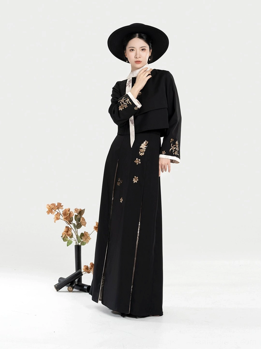 Front view of a black modern Hanfu two-piece outfit with golden phoenix-inspired floral embroidery, cropped stand-collar jacket, pleated skirt, and white contrast trim