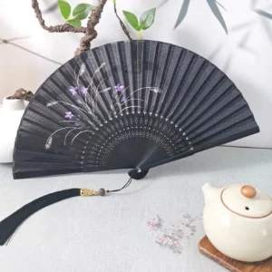 Black purple floral Chinese folding hand fan with hollow bamboo ribs and black tassel displayed on a Chinese tea table