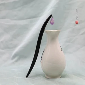 Black sandalwood amethyst Chinese hair stick displayed beside a white porcelain vase on a soft light fabric background