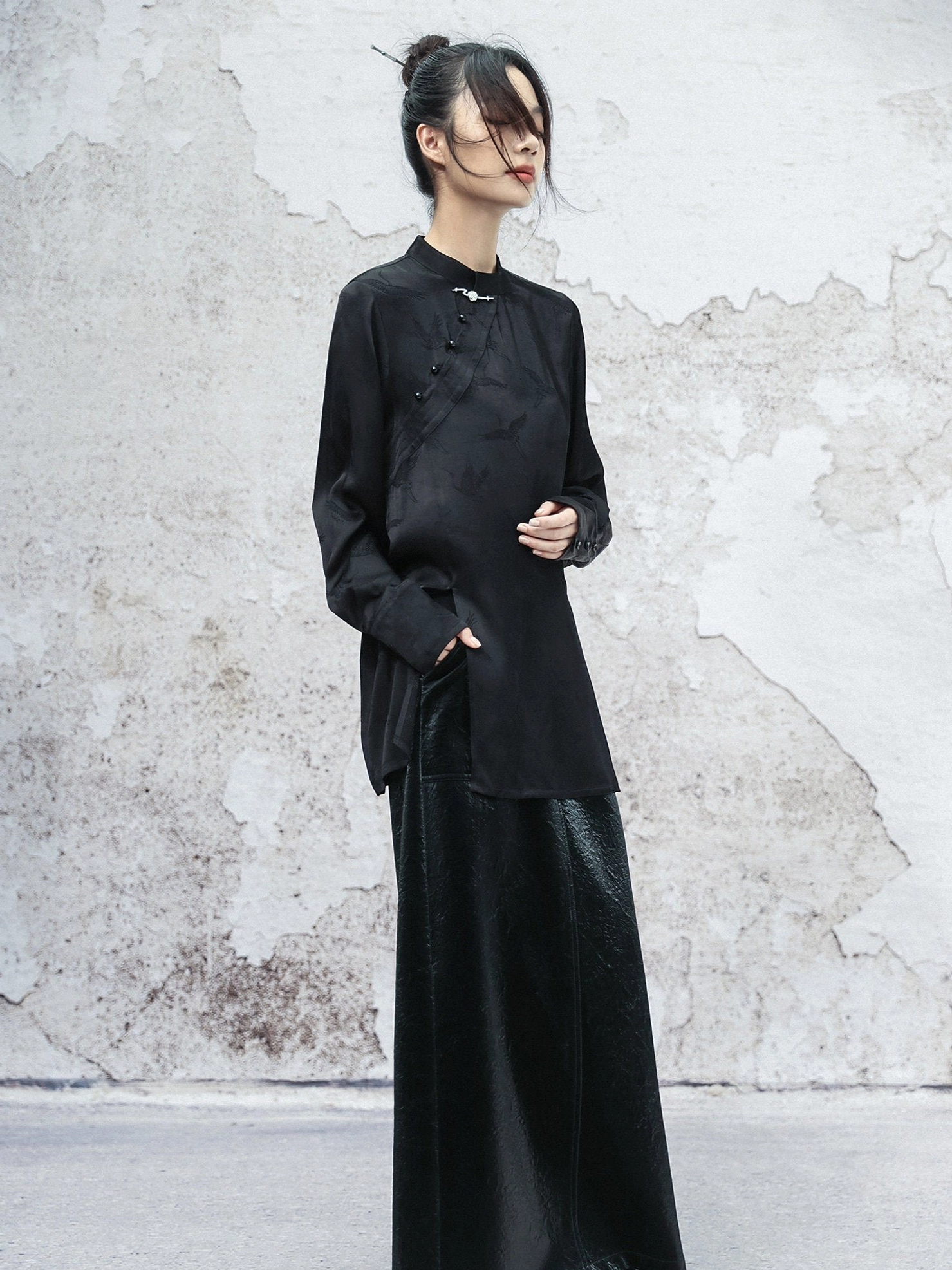 Back-side view of a relaxed black satin Hanfu-inspired long sleeve top with subtle woven pattern and buttoned cuffs styled with a long black skirt