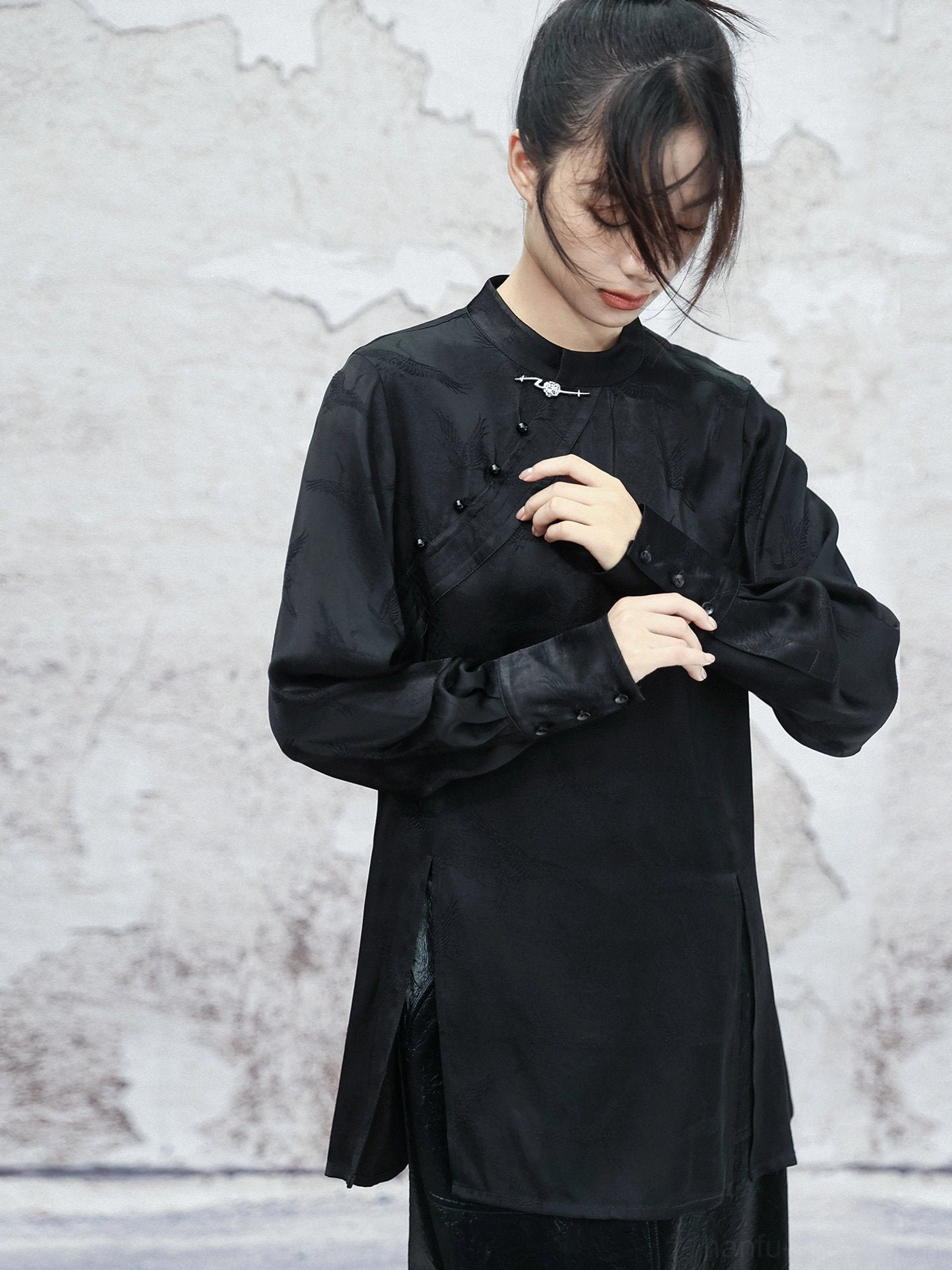 Detailed view of a black satin modern Chinese style Hanfu top with adjustable buttoned cuffs, frog button closure, side hem slits, and soft drape