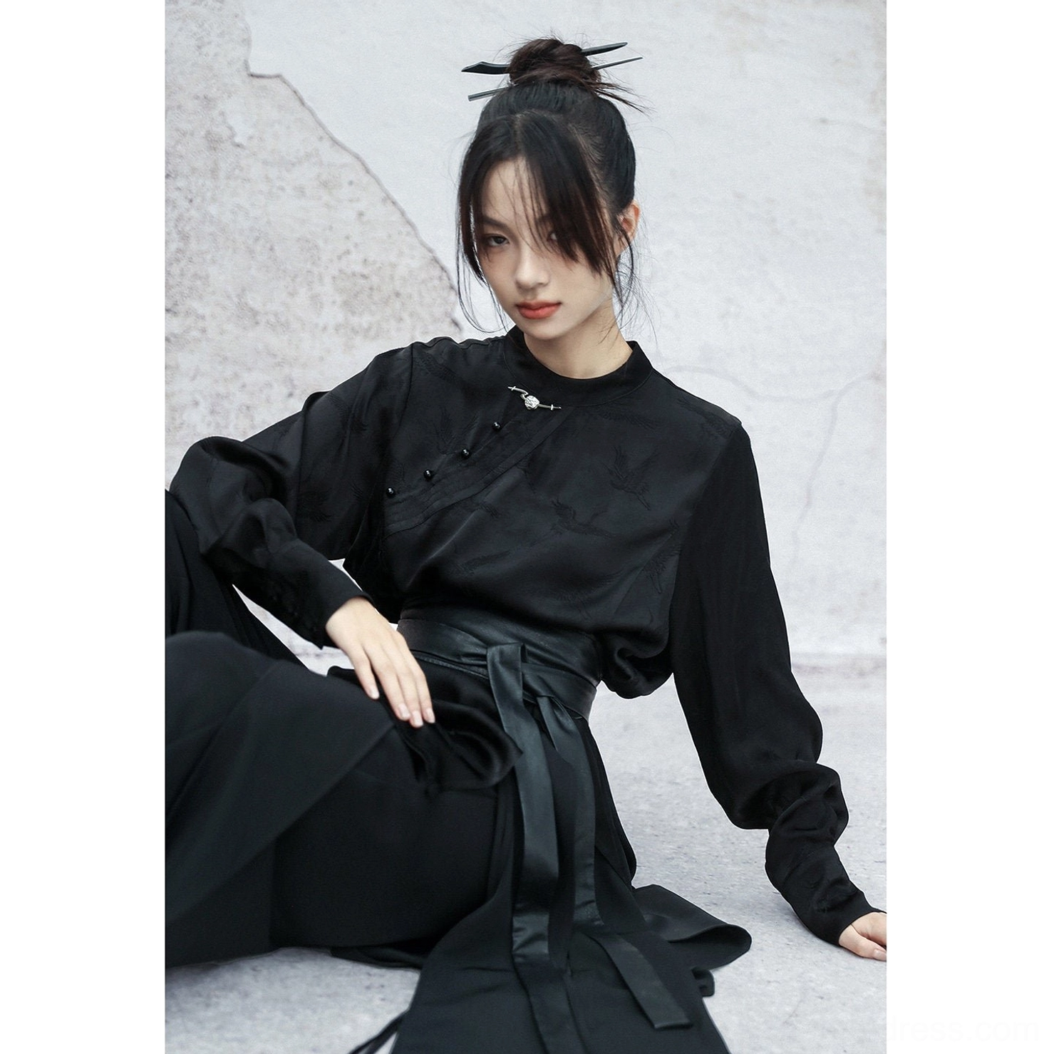 Front view of a black satin modern Hanfu long sleeve top with stand collar, frog buttons, subtle dark woven pattern, and relaxed fit styled with wide-leg trousers