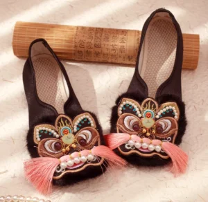 Three-quarter view of black Chinese Hanfu shoes featuring colorful tiger-head embroidery, pink tassel details, imitation pearl trim, furry toe caps, flexible rubber soles, and traditional styling
