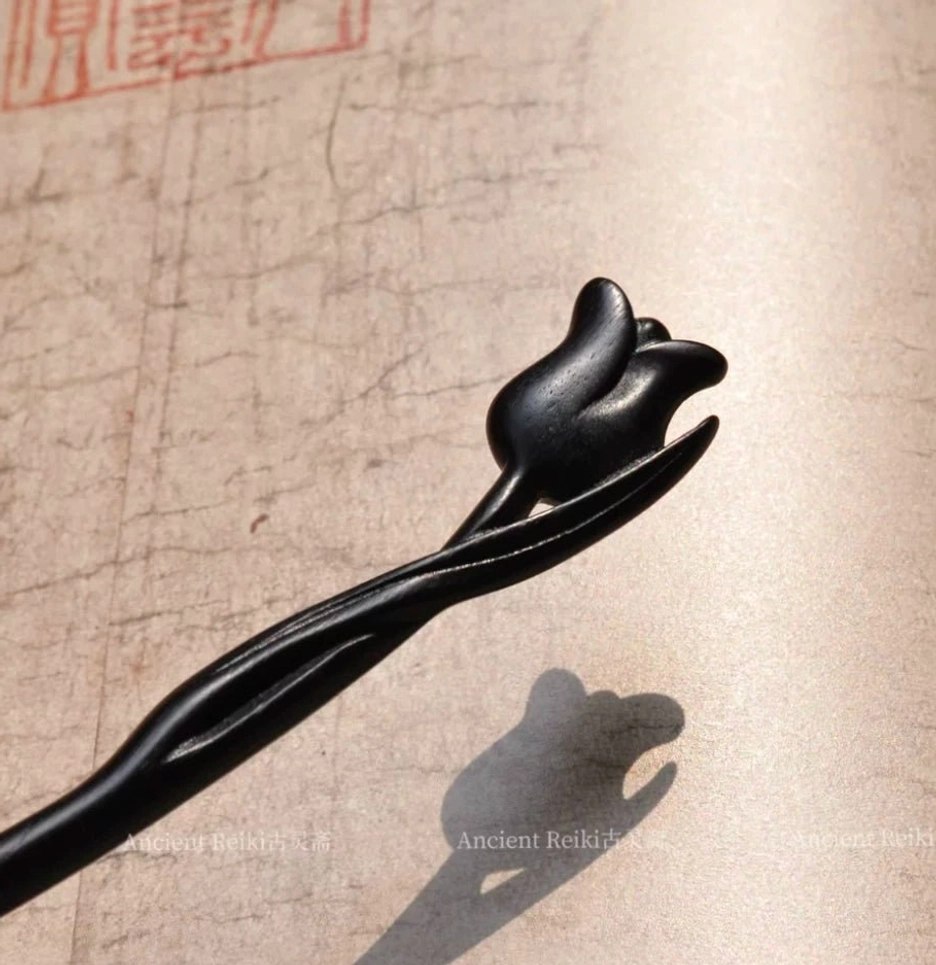 Close-up flat lay of a black tulip Chinese hair stick with carved flower detail and smooth curved stem on traditional Chinese paper