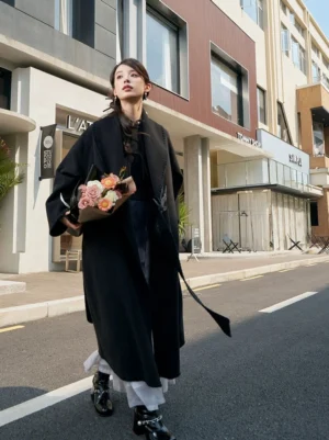 Black women's Chinese-style Hanfu robe coat with oversized fit, shawl collar, dark crane embroidery, waist sash, and long winter silhouette worn on a city street
