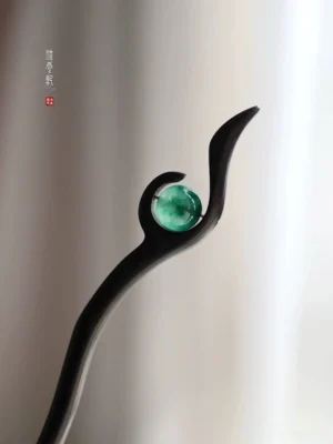 Black polished wood Chinese hair stick with round green jade ornament and graceful swirl-inspired curved top on a soft curtain background