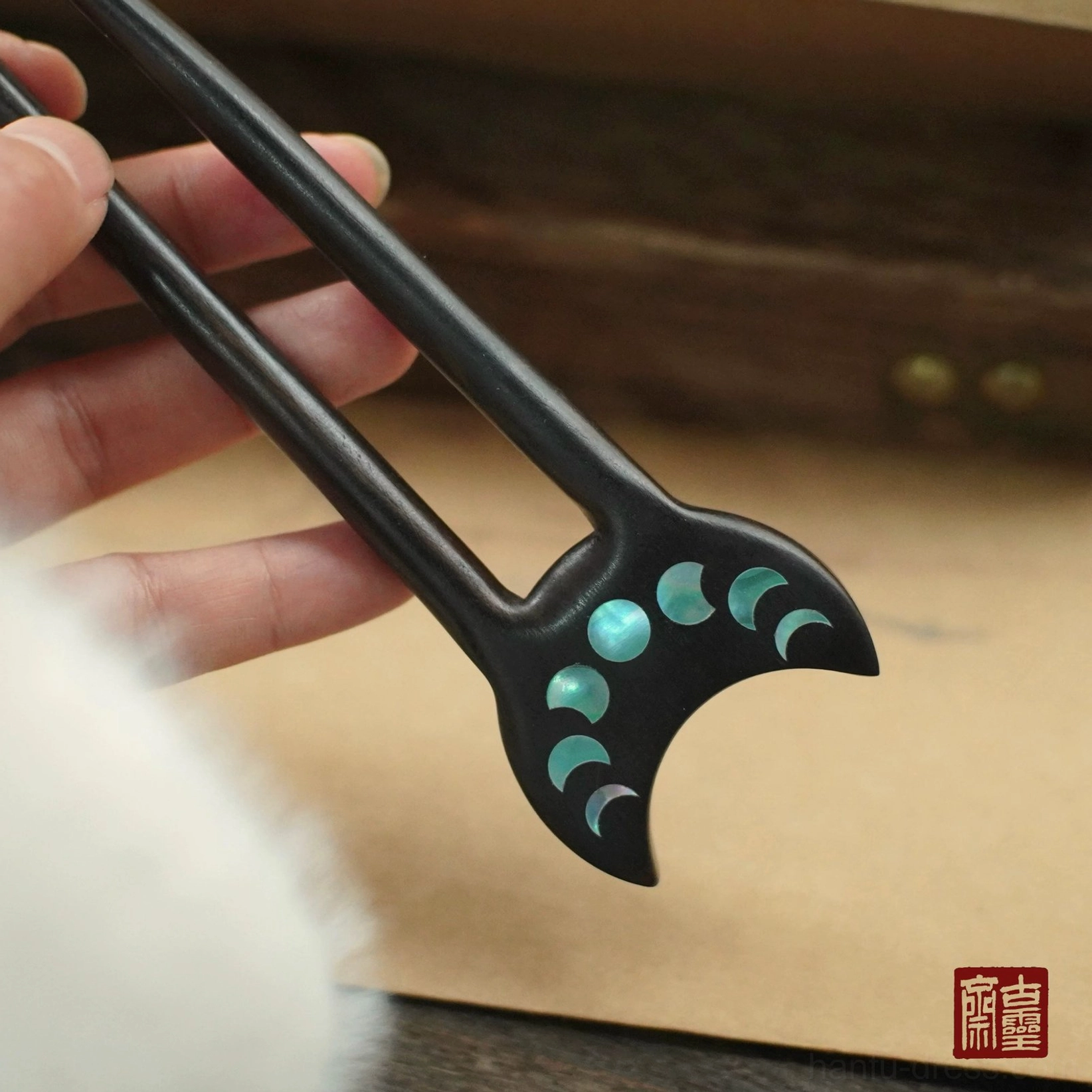 Close-up of polished black wooden Chinese hair stick featuring luminous cyan moon phase inlays for Hanfu and qipao styling