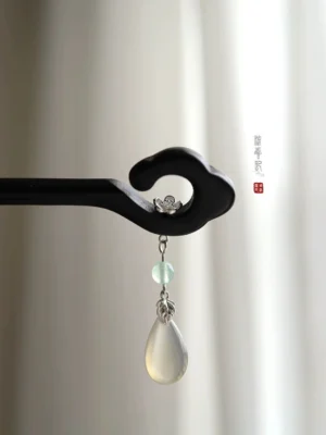 Side close-up of black wooden cloud Chinese hair stick with silver-tone flower ornament, green bead, and milky teardrop pendant