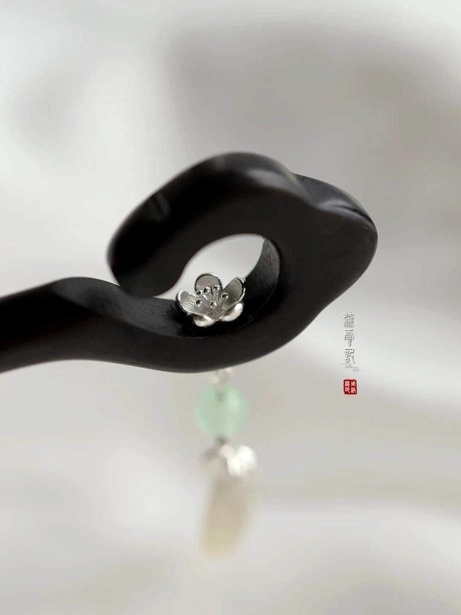 Macro close-up of silver-tone flower detail on black wooden traditional Chinese hair stick with green teardrop pendant