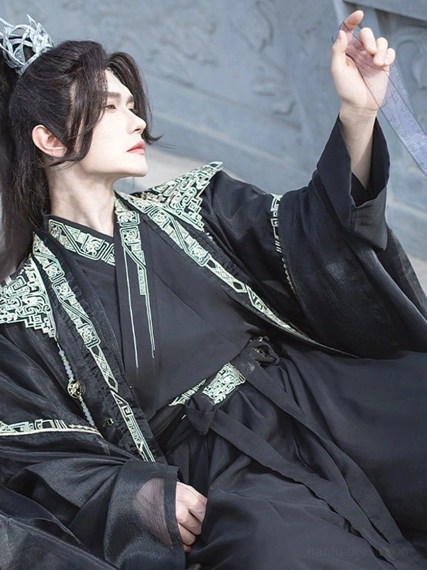 Close-up of black xianxia hanfu for men showing layered robes, flowing sash, wide sleeves, and intricate gold geometric collar trim