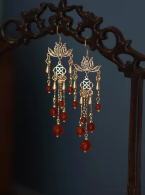 Blooming lotus red agate tassel earrings displayed on a carved dark wood jewelry rack, featuring hollow gold-tone lotus details and traditional Chinese Hanfu jewelry styling