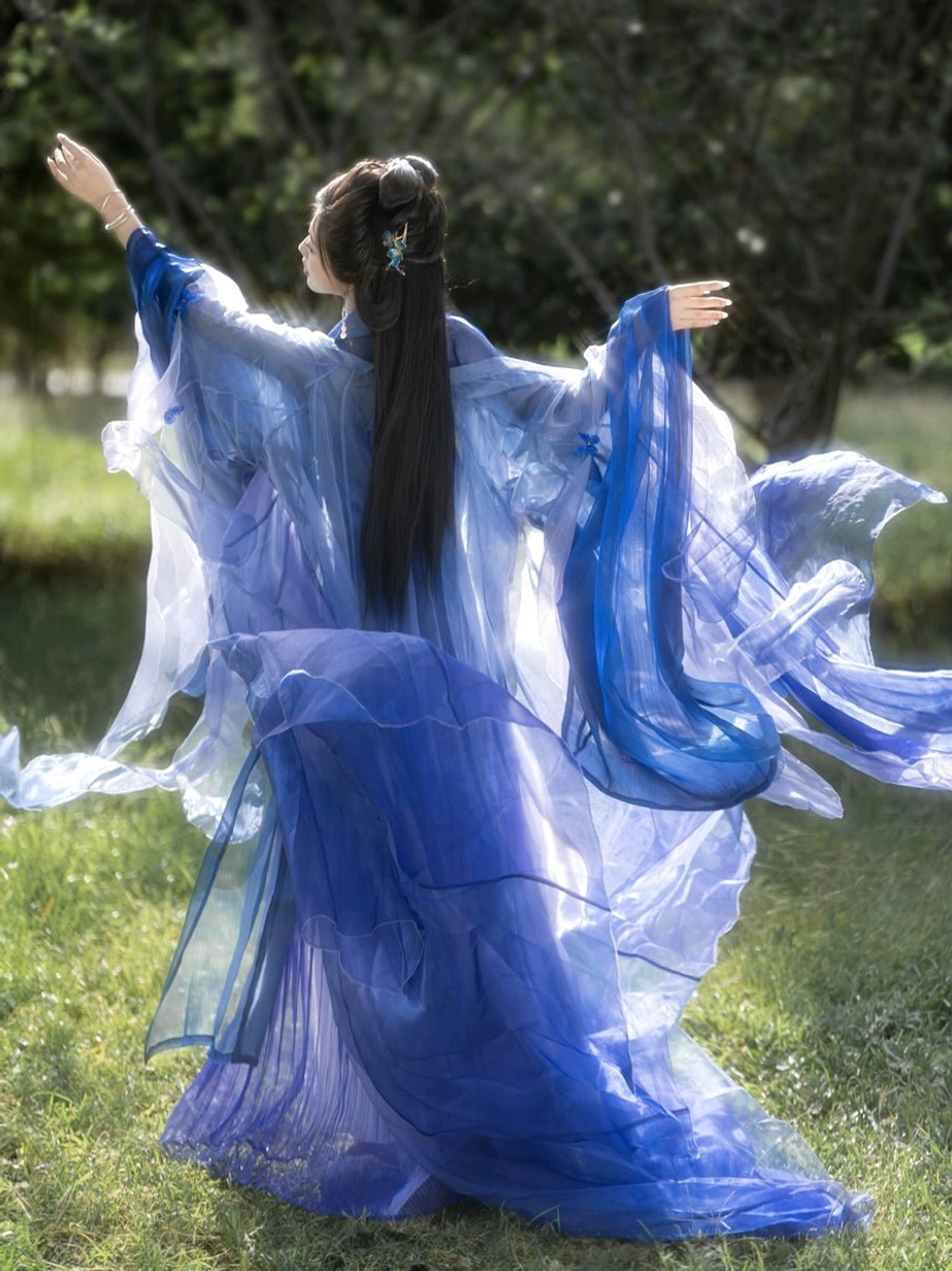 Blue butterfly themed Hanfu Heziqun shown from the rear with oversized sheer sleeves, wind-swept translucent blue fabric, floor-length pleated skirt, and elegant back drape