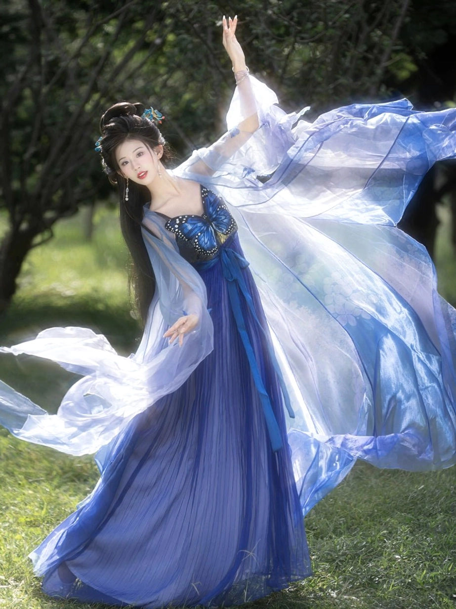 Illusory blue butterfly Tang Dynasty Hanfu Heziqun dress shown from a three-quarter front view with gradient blue sheer outer robe, butterfly chest embroidery, deep blue pleated skirt, and flowing sleeves in a sunlit woodland