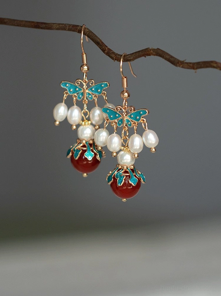 Blue cloisonne butterfly Chinese earrings with white pearl clusters and red agate drop pendants displayed on a natural branch