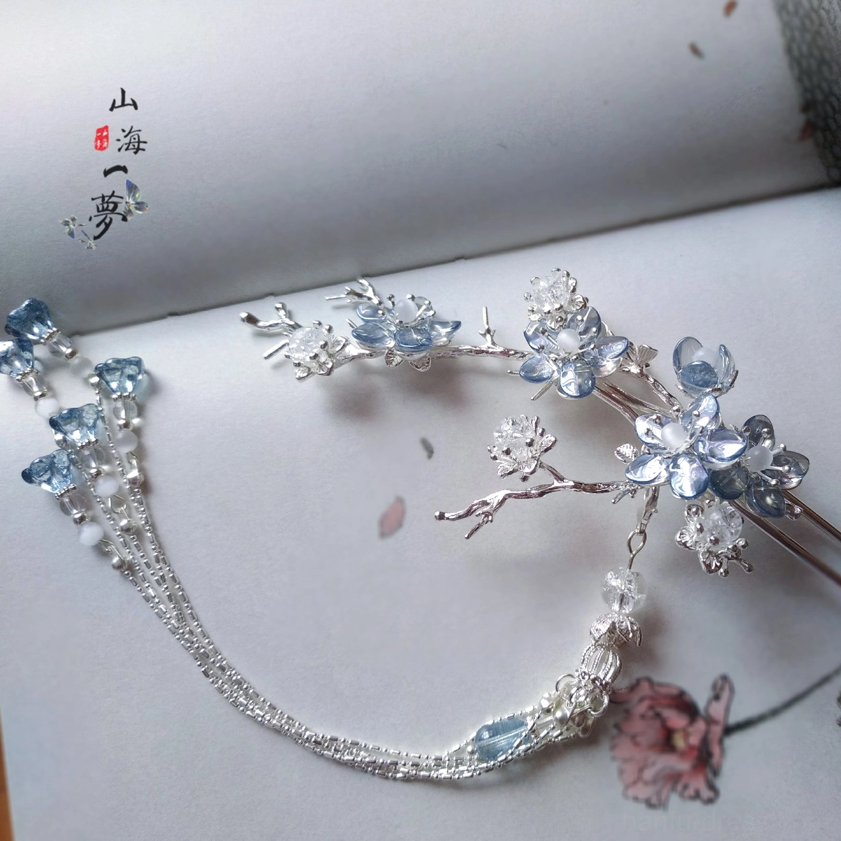 Blue crystal plum blossom hanfu hair ornament with silver branches and long tassels displayed on a vintage Chinese book page