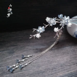 Blue crystal plum blossom hanfu hairpin with silver-tone branches and long layered tassels displayed on a dark wooden table