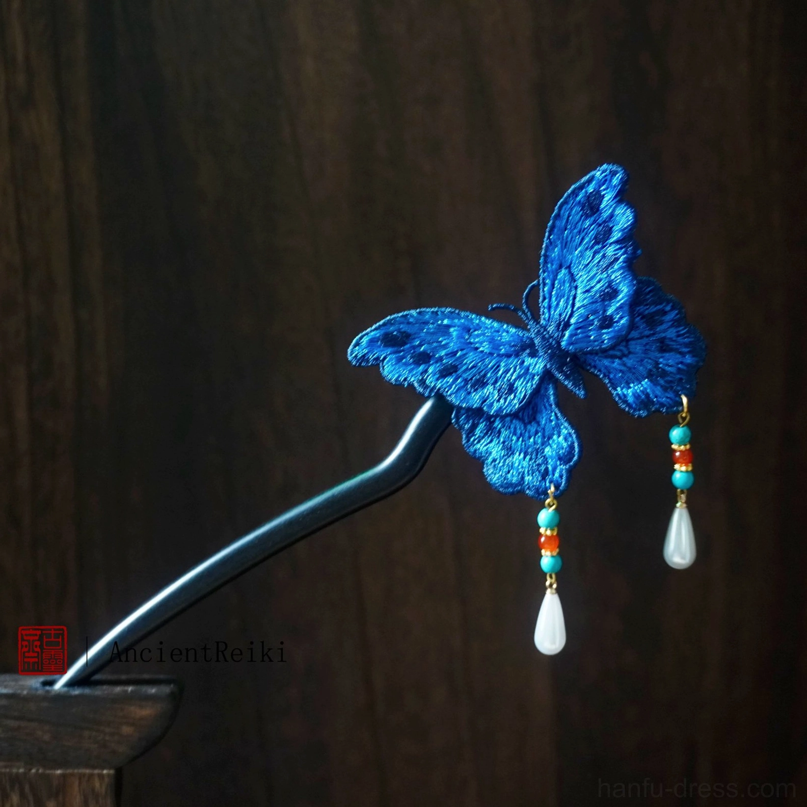 Blue embroidered butterfly Chinese hair stick with dark pin rod bead tassels and teardrop pendants on wood background