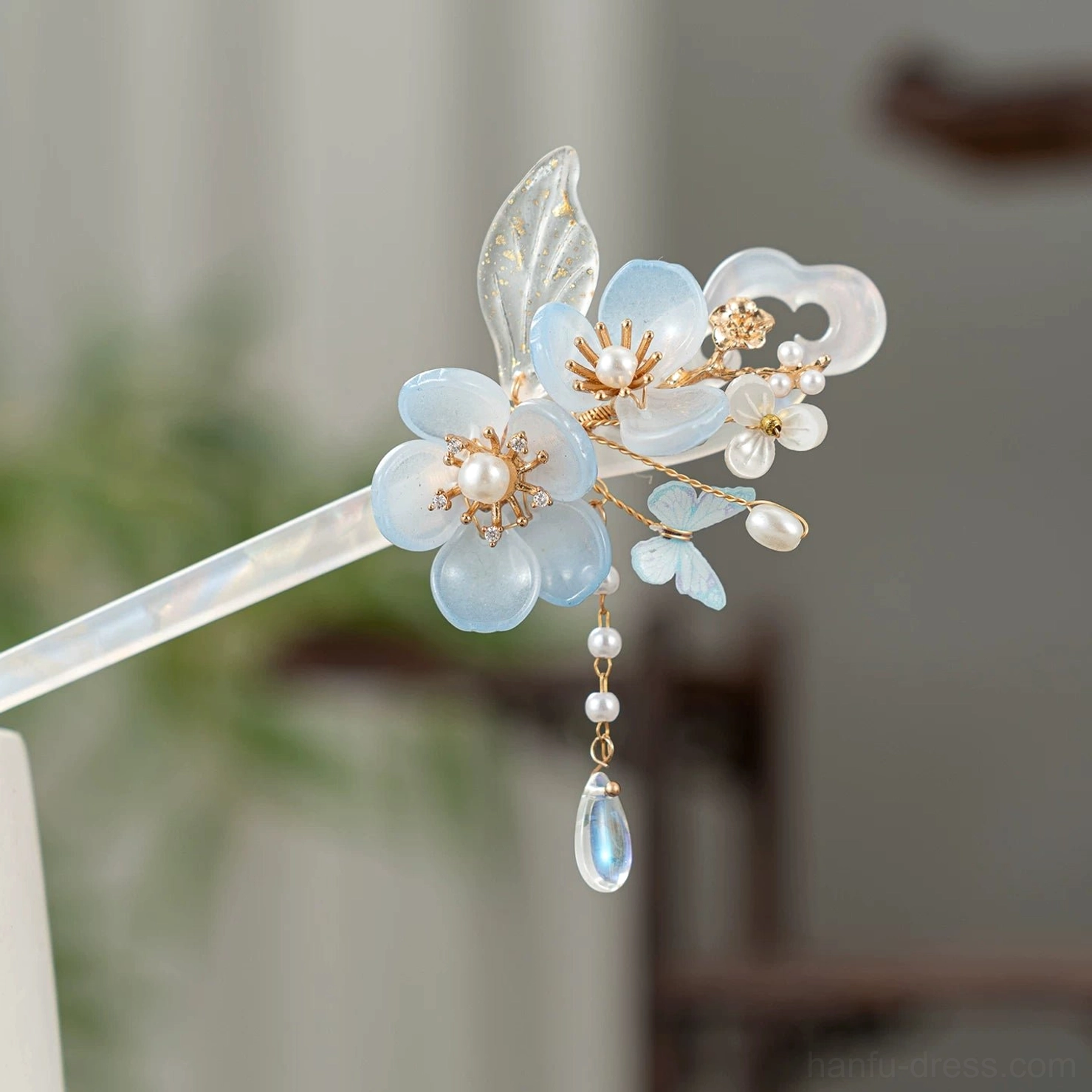 Side close-up of blue floral Hanfu hair stick featuring an iridescent white shaft, gold-tone accents, pearl-like beads, and blue glass tassel