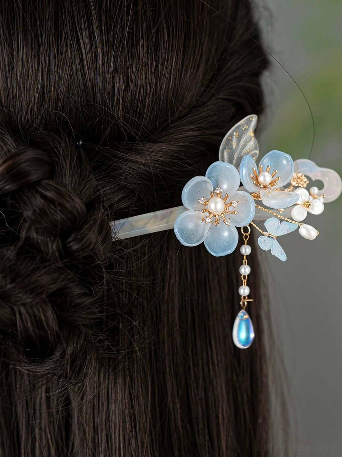 Blue floral Chinese hair stick worn in a braided updo, featuring an opalescent hairpin shaft, pearl-like beads, gold-tone details, and blue glass tassel