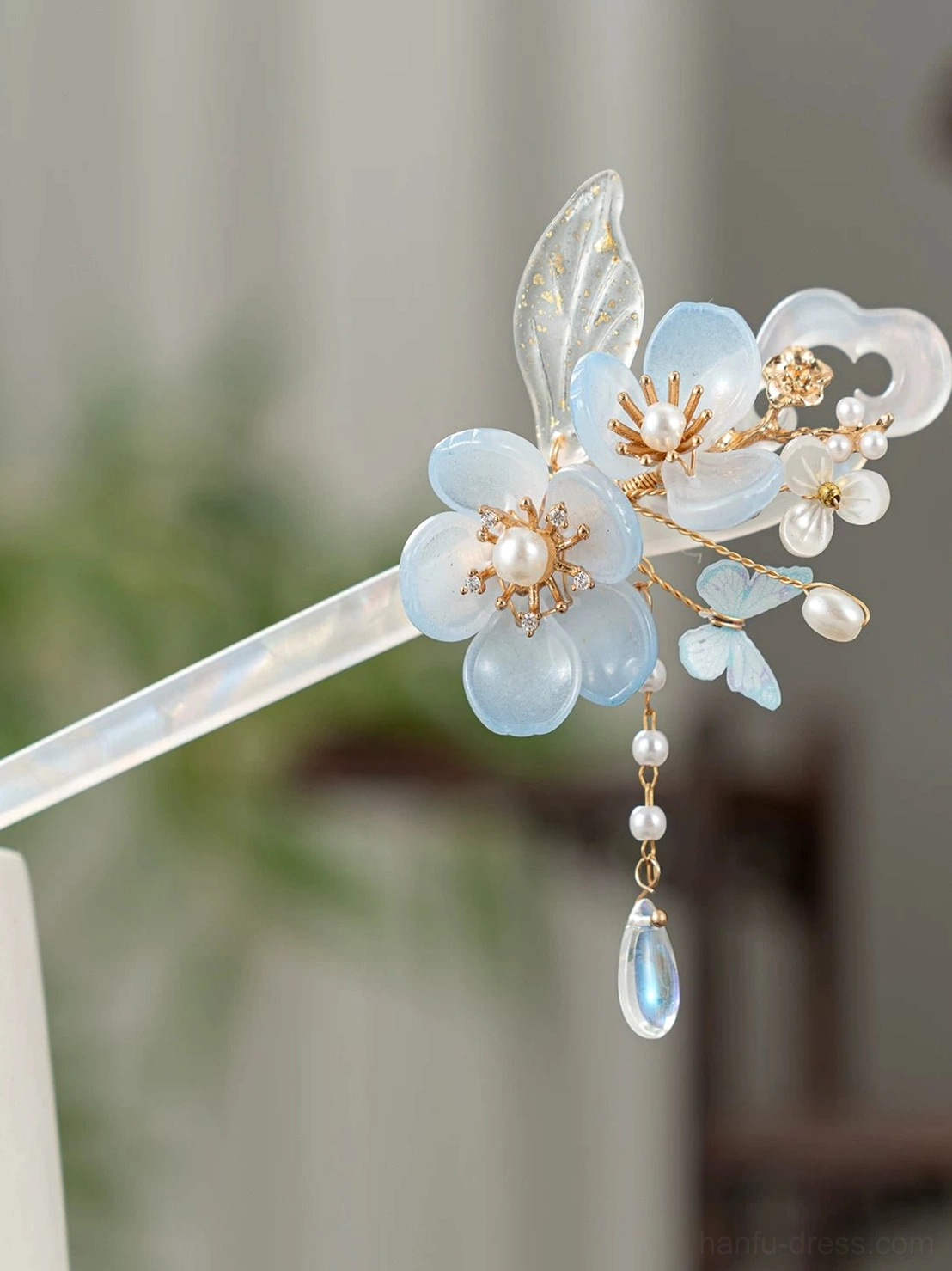 Front close-up of blue floral traditional Chinese hair stick with pearl-like bead clusters, gold-tone ornament, and blue drop tassel