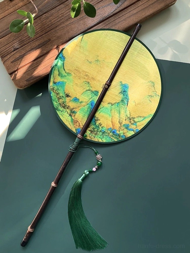 Chinese tuanshan round hand fan featuring blue green and golden mountain landscape painting, dark bamboo handle, green tassel, and decorative bead detail